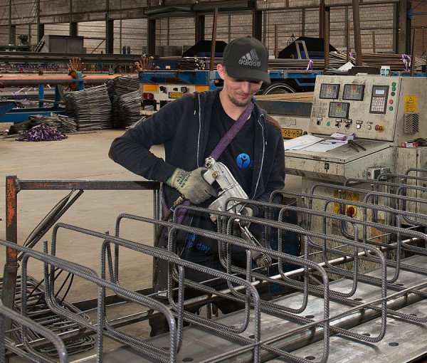 Een man werkt met staalwapening in een fabriekshal.