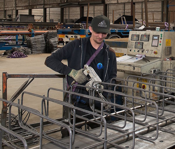 Medewerker assembleert stalen wapeningsnetten in een werkplaats.