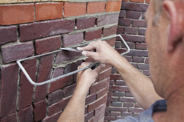 Vakman voegt bakstenen muur met handgereedschap.